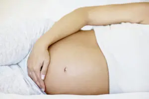 Mid section of a pregnant woman lying in bed , focus on her tummy