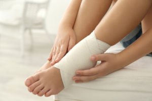 Little girl touching ankle with elastic bandage, close up view