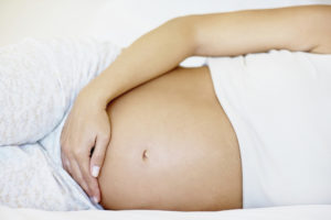 Mid section of a pregnant woman lying in bed , focus on her tummy